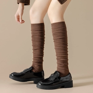 Dark brown ribbed knit over-knee socks styled with black loafers on a beige background
