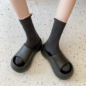 Detail of black platform open-toe slides made of EVA material worn with gray socks