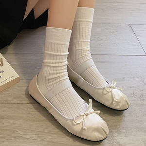 Top view of white ballet flats with bow and ribbed cotton socks on wood floor