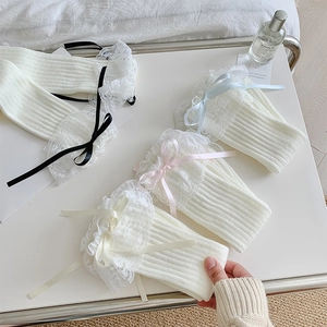 Dettaglio di scaldamuscoli in maglia bianca con pizzo delicato e fiocchi di nastro