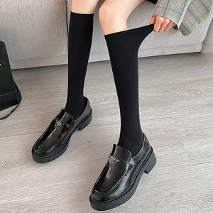Detail view of black knee high knitted socks worn with patent leather loafers