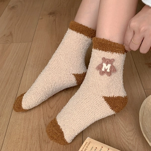 Close-up of fluffy coral fleece socks featuring a brown cartoon bear patch with M embroidery