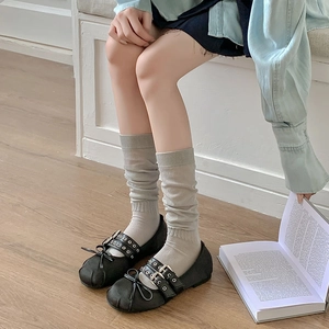Detail shot of light grey slouch socks paired with black Mary Jane shoes and a bow