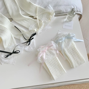 Dettaglio di scaldamuscoli in maglia bianco crema con pizzo e fiocchi di seta colorati