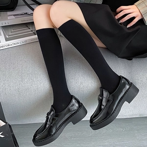 Detail of black glossy platform loafers and knit knee-high socks in Japanese school style
