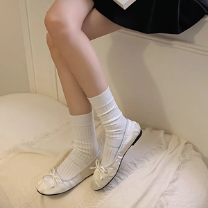 Close-up of white ballet flats with bow detail and matching ribbed crew socks