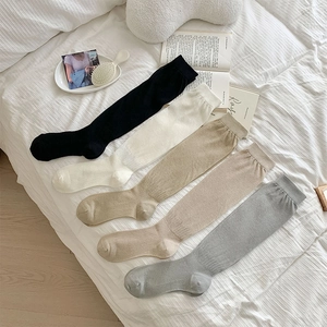 Five pairs of rib-knit knee-high socks in neutral colors like black and beige on a bed
