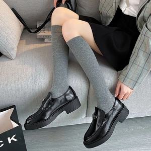 Detailed view of grey knitted knee-high socks paired with black platform leather loafers