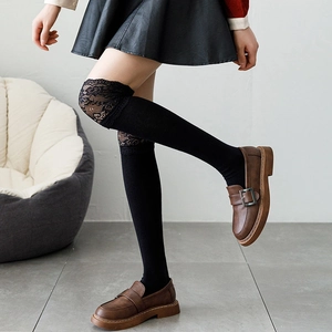 Detail of black over-the-knee socks with delicate lace trim and vintage loafers