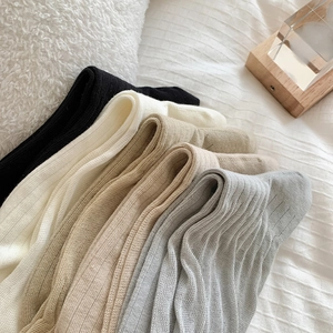 Détail de chaussettes hautes en maille côtelée en cinq couleurs neutres sur un lit