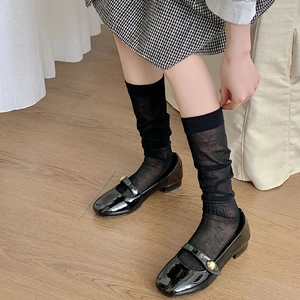 Detail of sheer black mesh socks paired with patent leather Mary Jane shoes and metal buckles