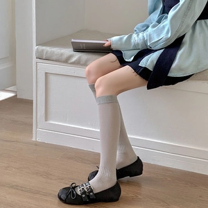 Detail of grey ribbed knit knee high socks paired with black Mary Jane shoes on white bench
