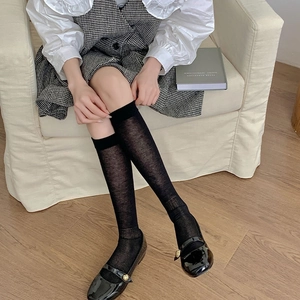 Close-up of sheer black knee-high socks with Mary Jane shoes on a cozy white sofa