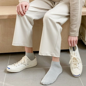 Close-up of light grey cotton sport socks with white canvas sneakers on a wooden bench