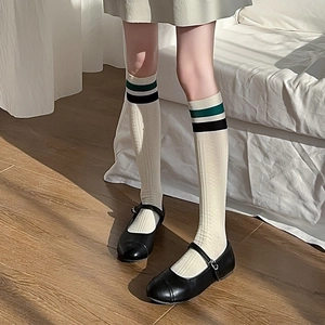 Detail of cream knee-high socks with green stripes and ribbed texture on the leg