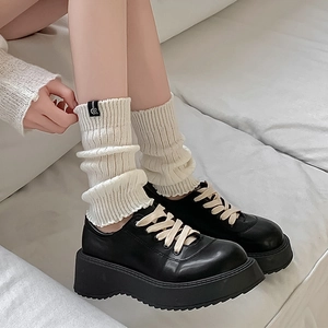 Close-up of white knitted slouch socks paired with black platform lace-up leather shoes