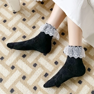 Detail of black mid-calf socks featuring white floral lace cuffs and subtle knit textures