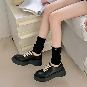 Close-up of black knit leg warmers paired with platform oxford shoes in a cozy setting