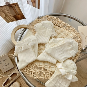 Detail view of cream lace socks with satin bows and hollow knit patterns in a woven tray