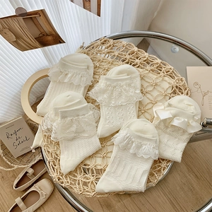 Detail of five pairs of off-white lace socks with bows and frills on a vintage table