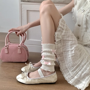 Détail de jambières en maille crème avec des nœuds roses au style balletcore