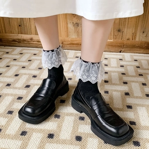 Close-up of white floral embroidery lace edge on socks with black platform loafer shoes