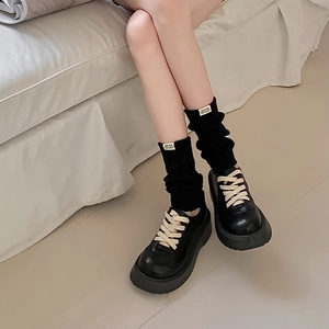 Detail of black knit leg warmers with label paired with platform matte leather shoes