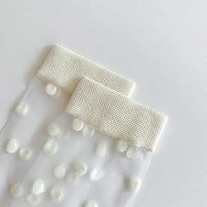 Detail of white semi-transparent knee-high socks featuring textured polka dots and ribbed cuffs
