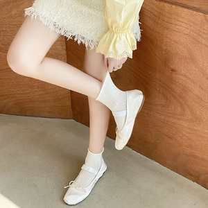 Close-up of cream Mary Jane ballet flats with mesh socks and bow detail on a wood floor