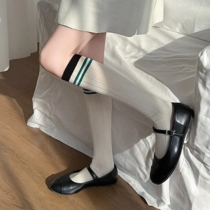 Detail of white ribbed knee-high socks with green stripes and black Mary Jane shoes
