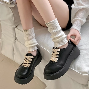 Detail of black platform leather loafers paired with white ribbed knit leg warmers