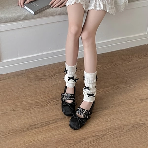 Gros plan de jambières en tricot blanc avec nœuds en satin noir et chaussures Mary Jane