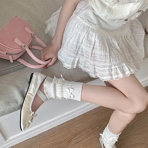 Détail des jambières tricotées blanches avec nœuds en soie et ballerines Mary Jane