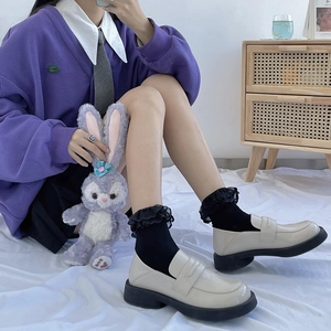 Close-up of cream patent leather platform loafers with black lace socks in school style
