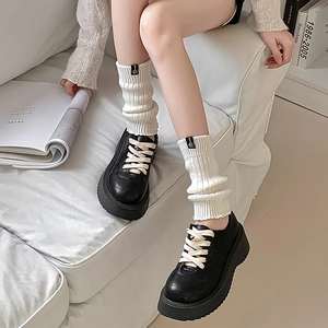 Close-up of white ribbed knit leg warmers with logo tag paired with black platform shoes