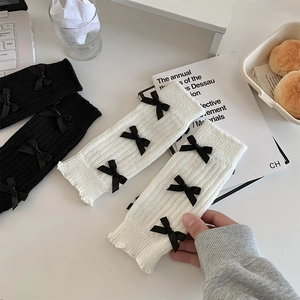 Détail de jambières en maille côtelée blanche et noire avec nœuds en ruban satin
