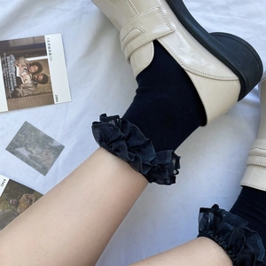 Detail of black mid-calf socks with organza ruffles worn with white platform loafers