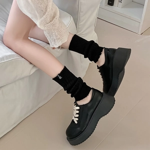 Detail of black knit leg warmers with white letter embroidery paired with platform shoes