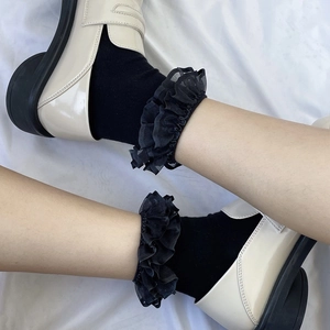 Close-up of Lolita style black lace ruffled socks paired with beige loafers on white fabric