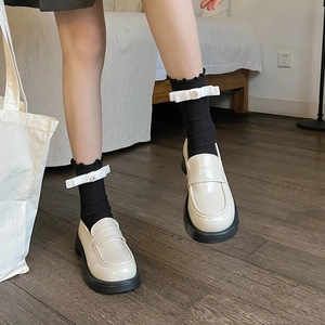 Close-up of white patent loafers with platform soles and black bow ruffle mid-tube socks