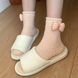 Detail of coral fleece socks with plaid bows paired with open-toe home slippers