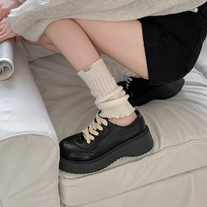 Detail of cream knit leg warmers paired with black platform oxfords on a white sofa