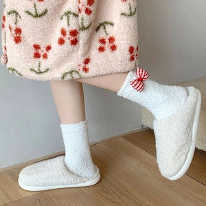 Detail of white plush socks with red striped bowknot and soft coral fleece texture