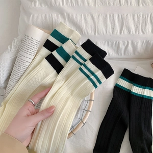 Detail of white rib-knit knee-high socks with vintage green stripes in academic style