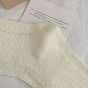 Detailed macro view of white knee-high socks with argyle knit texture and striped cuffs