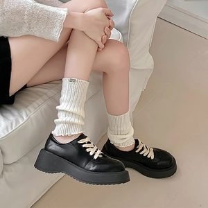 Detail of off-white knitted leg warmers with logo tag and black platform leather shoes