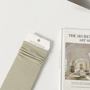 Detail of light green ribbed knee-high socks with branded tag and minimalist magazine background
