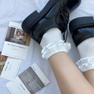 Detail of white double-layered lace ruffle socks paired with black round-toe shoes