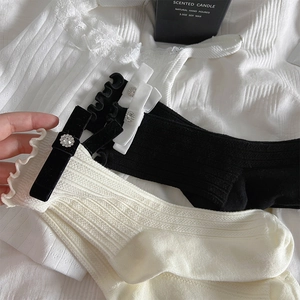 Detail of ruffled cuff socks with velvet bow and rhinestone accent in black and cream