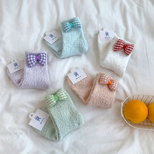 Close-up of five pairs of warm coral fleece socks with plaid bows on a white fabric background